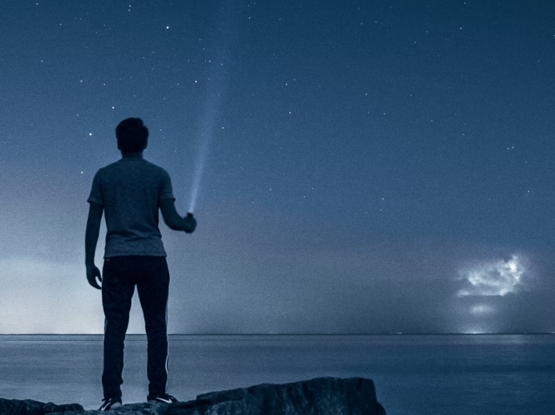 man looking at stars with flashlight