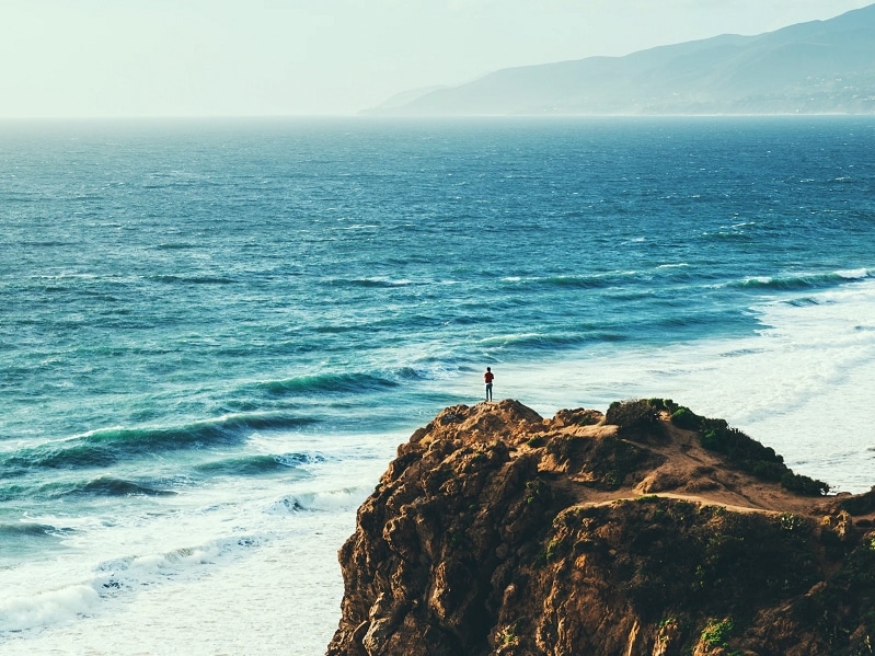 person standing on cliff waves ocean sea