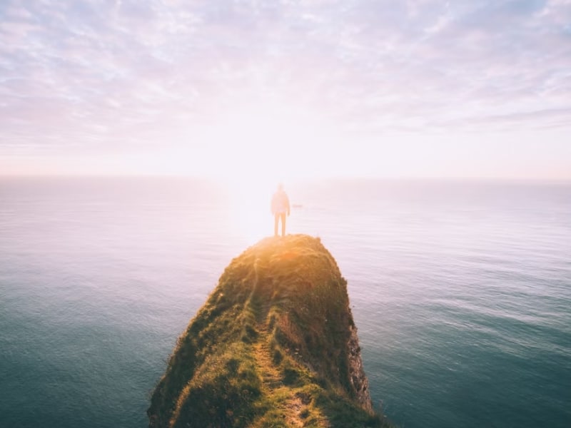 person standing on edge of cliff ocean