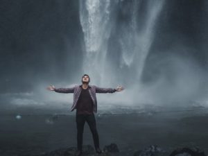 man opening up in front of waterfall