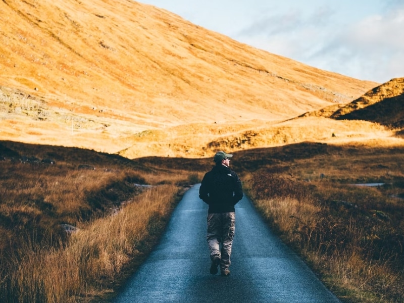 man walking road through hills