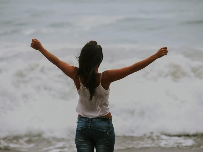 woman opening arms at beach waves