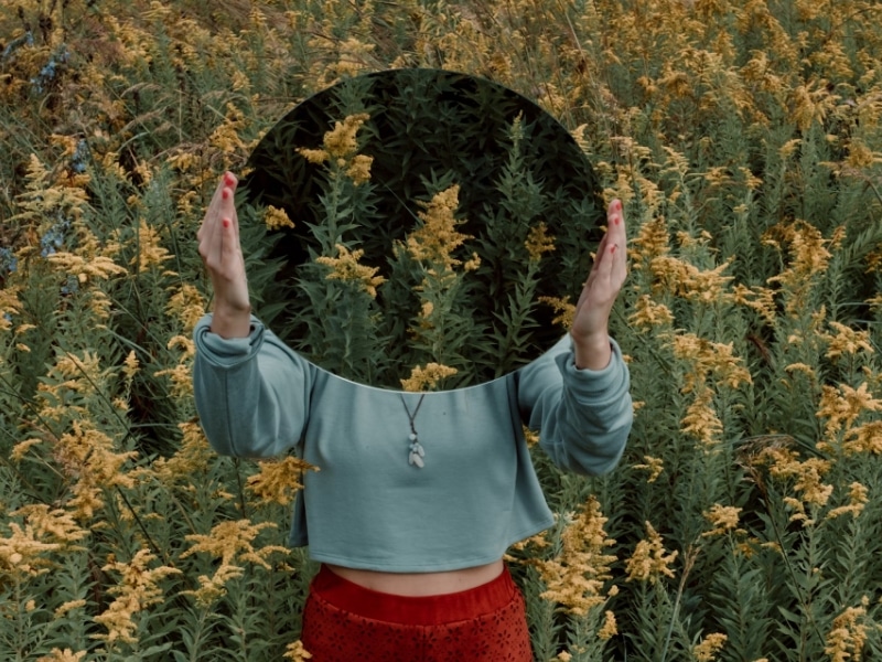 woman holding mirror in field of flowers