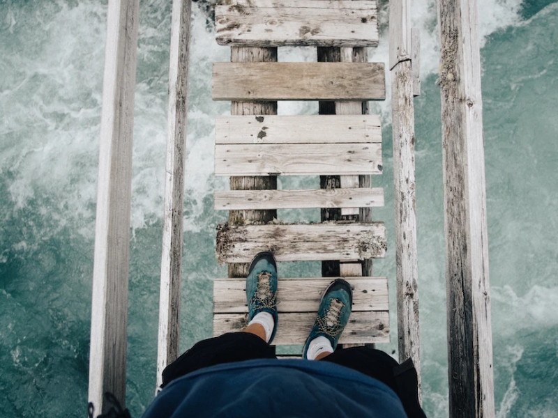 person looking down on suspension bridge above water